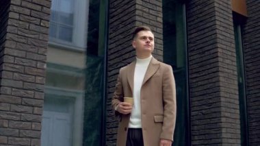 Kahverengi paltolu yakışıklı iş adamı, ofisin yanında kahve var.