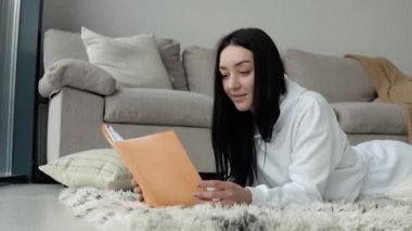 Oturma odasında yerde kitap okuyan, kitap okuyan genç bir kadın. Evde kal konsepti