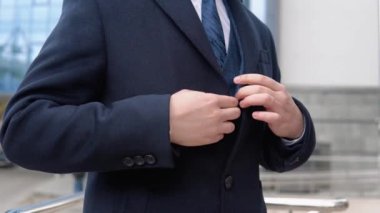 Ceketinin düğmelerini ilikleyen bir adamın yakın çekimi. Ofis merkezine yakın mavi ceketli ve ceketli genç, zarif erkek işadamı.