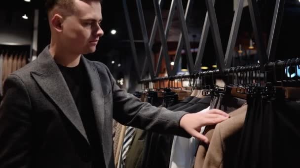 Νεαρός με αυτοπεποίθηση άντρας σε μπουτίκ πολυτελείας διαλέγει νέο κοστούμι. Κατάστημα ρούχων Mens — Αρχείο Βίντεο