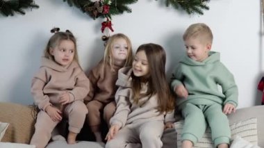 Dost canlısı çocuklar Noel ve yeni yıl süslemelerinin yakınında koltuğun arkasında otururlar.