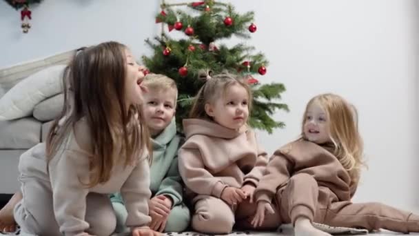 Niños juguetones se sientan cerca del árbol de Navidad — Vídeos de Stock