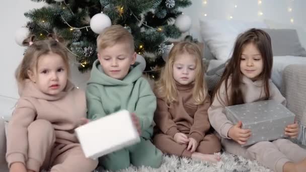 Niños sentados cerca del árbol de Navidad y compartiendo sus regalos — Vídeos de Stock
