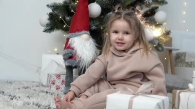 Tatlı küçük kız Noel ağacının yanında oturuyor.