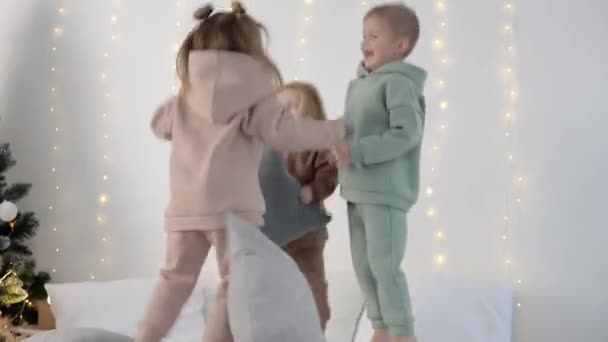 Gyerekek ugrál az ágyon párnák közelében karácsonyi dekorációk — Stock videók