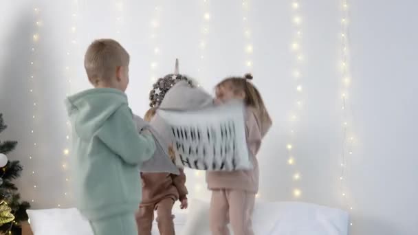 Çocuklar Noel süslemelerine yakın yastıklarla yatakta zıplıyorlar. — Stok video