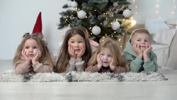 Tatlı çocuklar Noel ağacının önünde uzanıp bacaklarını sallıyorlar. Ön Wiew — Stok video