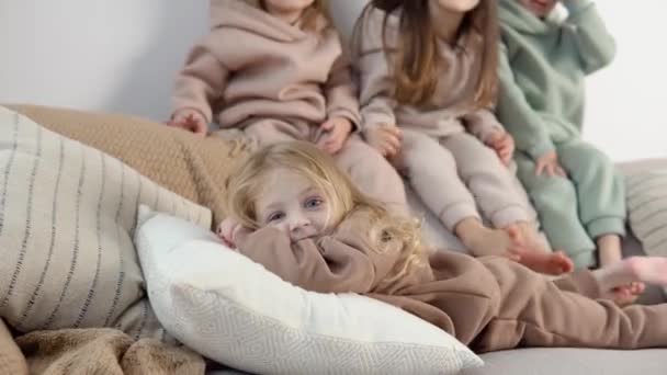 La chica se acuesta cómodamente sobre una almohada. Niños simpáticos se sientan en la parte posterior del sofá cerca de las decoraciones de Navidad y Año Nuevo — Vídeos de Stock