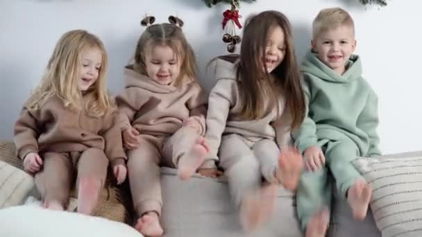 Niños simpáticos se sientan en la parte posterior del sofá y juegan cerca de las decoraciones de Navidad y Año Nuevo — Vídeos de Stock