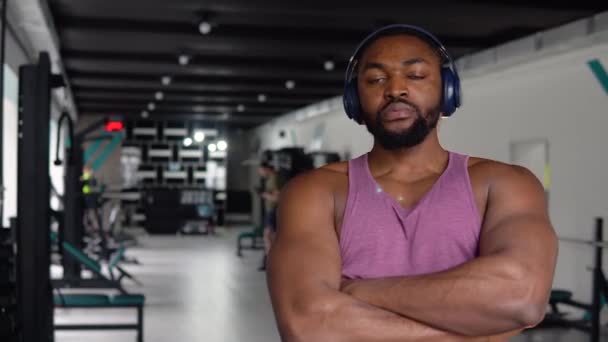 Homem negro com fones de ouvido olhando para a câmera no ginásio — Vídeo de Stock
