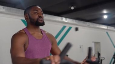 Afrika kökenli Amerikalı sakallı adam spor salonunda velosimulator üzerinde çalışıyor.