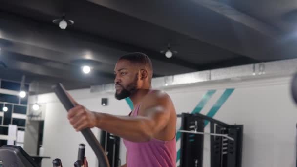 Svart mann trener på elliptisk trener i gymsalen – stockvideo