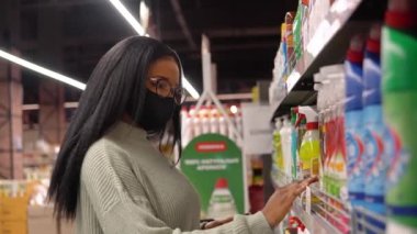Maskeli kız süpermarketteki raflardan ürünleri seçiyor.