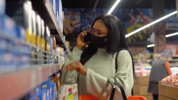 Dziewczyna w masce wybiera produkty na półkach w supermarkecie — Wideo stockowe