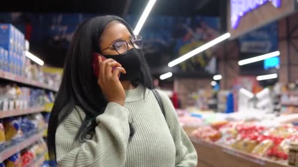 Fille dans un masque parler au téléphone dans le supermarché — Video