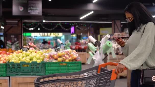 Menina com uma máscara falando no telefone no supermercado — Vídeo de Stock