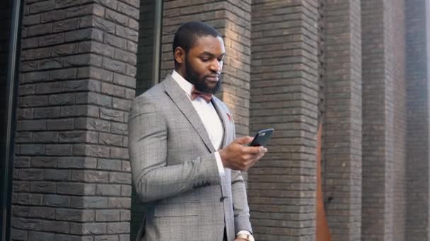 Jovem e elegante empresário afro-americano falando ao telefone perto do centro de escritórios — Vídeo de Stock