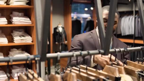 Szakállas, magabiztos afro-amerikai férfi luxusruhás butikban, új öltönyt választ. Férfi ruhaüzlet — Stock videók