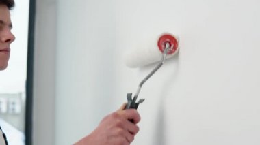 Ressam beyaz duvarları boya silgisiyle boyuyor.