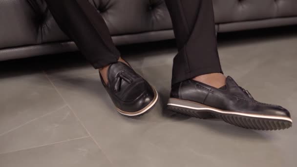 Κοντινό πλάνο των κομψών παπούτσια mans όταν ο άνθρωπος κάθεται σε έναν καναπέ — Αρχείο Βίντεο