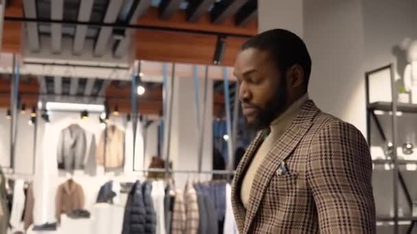 Mladý sebevědomý muž v luxusním pánském butiku si vybírá nový oblek. Pánské oblečení obchod — Stock video