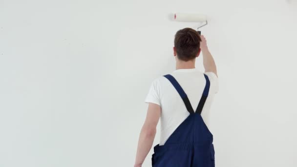 O pintor com um rolo nas mãos pinta uma parede branca. Vista de trás — Vídeo de Stock