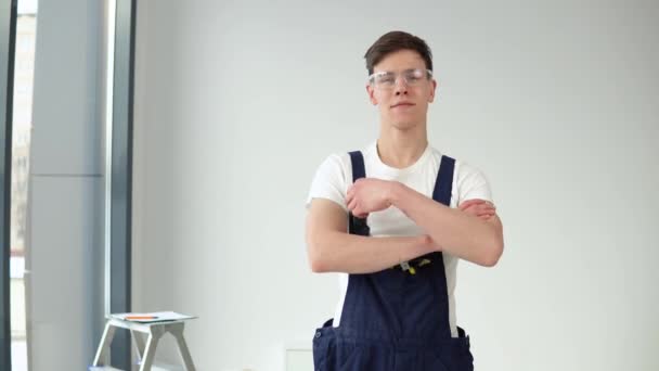 Jeune maître en uniforme de travail et lunettes de protection regardant la caméra — Video