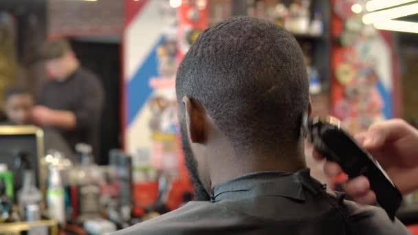 Парикмахер стрижет волосы клиентов стрижкой для волос. Крупный план и вид сзади — стоковое видео