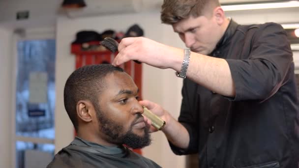 Cabeleireiro jovem corta jovem na barbearia. Roupas pretas. Pessoas internacionais — Vídeo de Stock