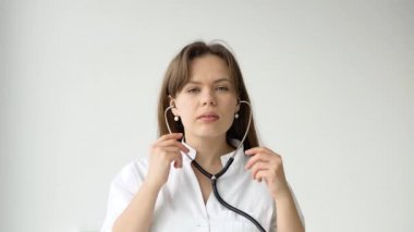 Beyaz ceketli ve steteskoplu beyaz kadın doktor kameraya bakıyor. Hastane ofisinde poz veren gülümseyen kadın doktor.