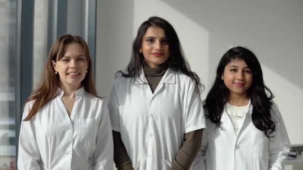 Três jovens médicas de diferentes nacionalidades olham para a câmera — Vídeo de Stock