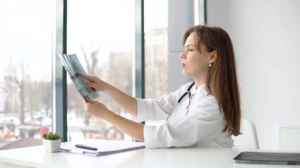 Jonge blanke vrouw arts draagt witte medische jas en stethoscoop houdt de x-ray — Stockvideo