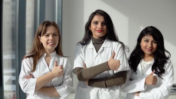 Studenten geneeskunde stagiaires van verschillende nationaliteiten kijken in de camera en tonen een teken van ca. Artsen team — Stockvideo
