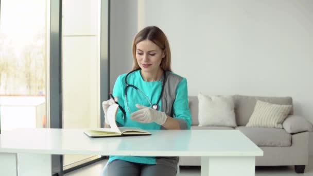 Female doctor wearing medical coat and stethoscope writes a medical history in a notebook — Stock Video