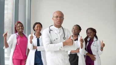 Afrikalı bir doktor ve hemşire kameranın önünde dikilip ileriye bakıyor.