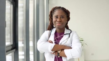 Afrika kökenli Amerikalı kadın doktor ya da hemşire klinikte tıp kıyafeti içinde kameraya bakıyor.
