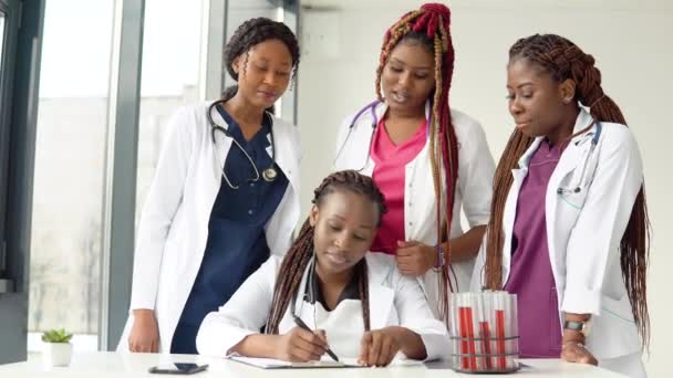Jonge artsen hebben een discussie aan tafel terwijl een van hen aantekeningen maakt. — Stockvideo
