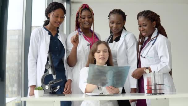 Los médicos jóvenes examinan una radiografía mientras están de pie en una mesa — Vídeo de stock