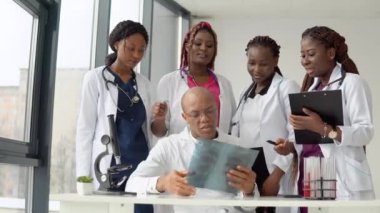 Beş Afrikalı Amerikalı doktor erkek ve kadın bir masada dururken röntgen çekiyorlar.