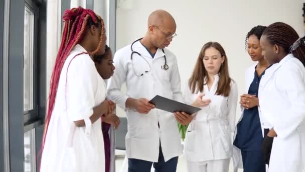 Un equipo de médicos, incluidos hombres y mujeres internacionales, mantienen una conversación de negocios mientras están en una clínica — Vídeo de stock