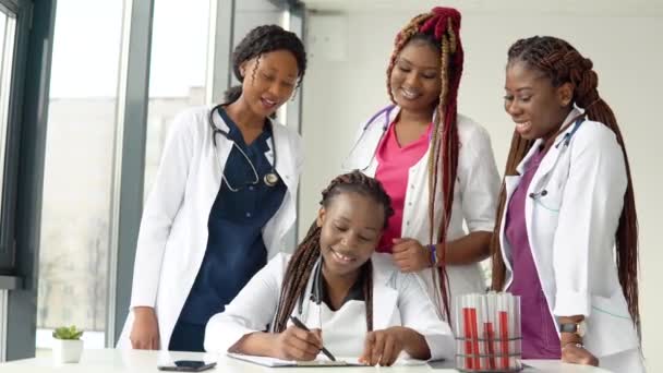Genç Afro-Amerikan doktorlar, bir tanesi notlar alırken masada oturup tartışıyorlar. — Stok video