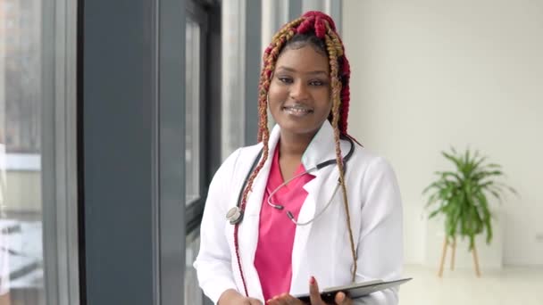 Afroamerikanische Ärztin mit roten Haaren oder Krankenschwester steht im Anzug in der Klinik und blickt in die Kamera — Stockvideo