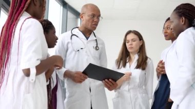 Aralarında uluslararası erkek ve kadınların da bulunduğu bir grup doktor, klinikte dururken iş görüşmesi yapıyor.
