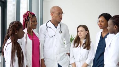 Aralarında uluslararası erkek ve kadınların da bulunduğu bir grup doktor, klinikte dururken iş görüşmesi yapıyor.
