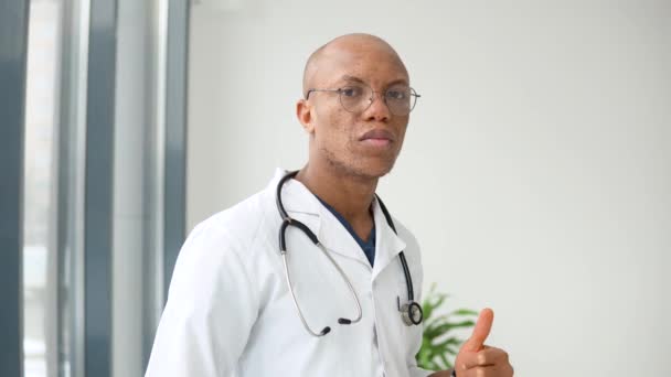 Seorang dokter muda afrika Amerika berdiri dalam setelan medis di klinik dan melihat kamera — Stok Video