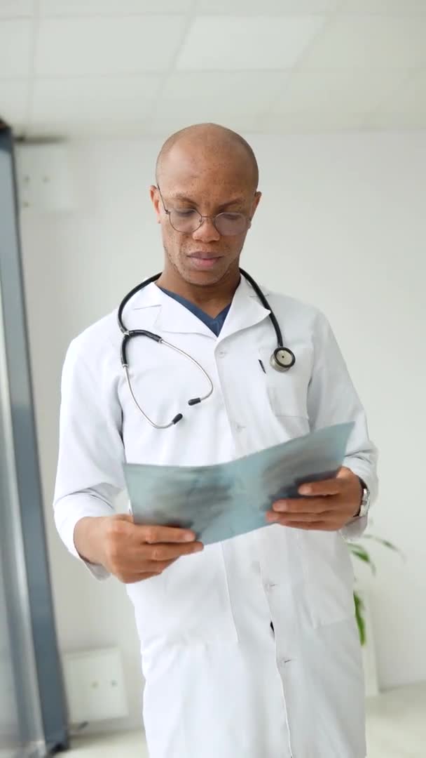 若いアフリカ系アメリカ人の医師が診療所に立ち、カメラを見ている。垂直ビデオ — ストック動画