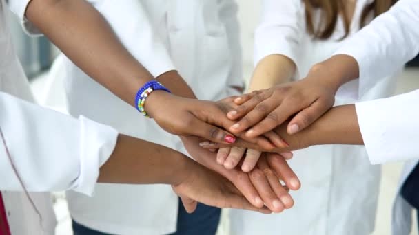 Un equipo de médicos, incluyendo mujeres y hombres de diferentes nacionalidades, hacen un gesto de unidad. Primer plano de disparo de manos — Vídeo de stock