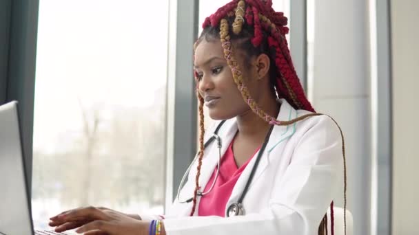 Νεαρή αφροαμερικανίδα γιατρός που εργάζεται σε φορητό υπολογιστή στη σύγχρονη κλινική — Αρχείο Βίντεο