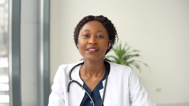 Junge afrikanisch-amerikanische Ärztin plaudert oder berät sich am Laptop und blickt direkt in die Kamera — Stockvideo