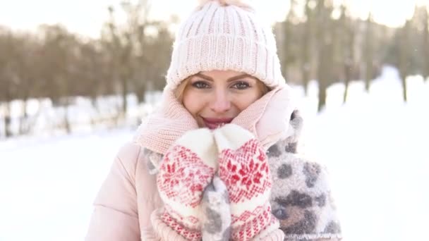 Vacker ung kvinna i en mjuk rosa dunjacka, vit hatt, vantar och halsduk på en bakgrund av snöiga landskap — Stockvideo